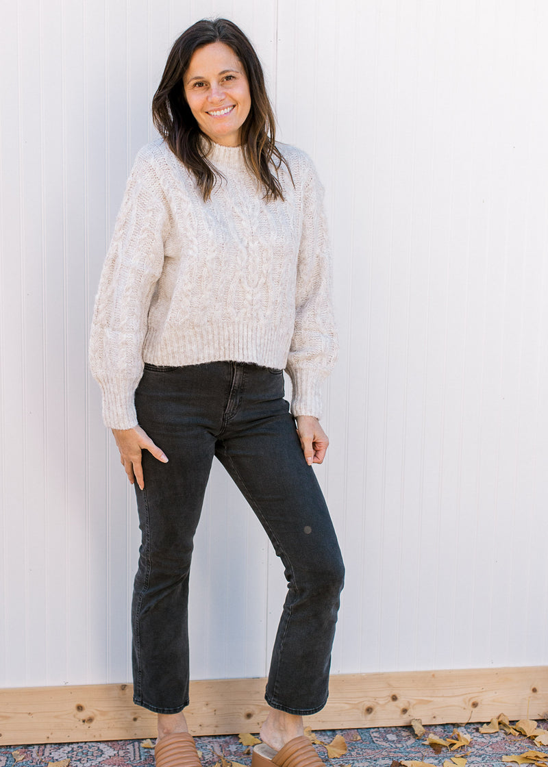 Model wearing jeans, mules and a cream sweater with long sleeves, mock neck and a cropped fit. 