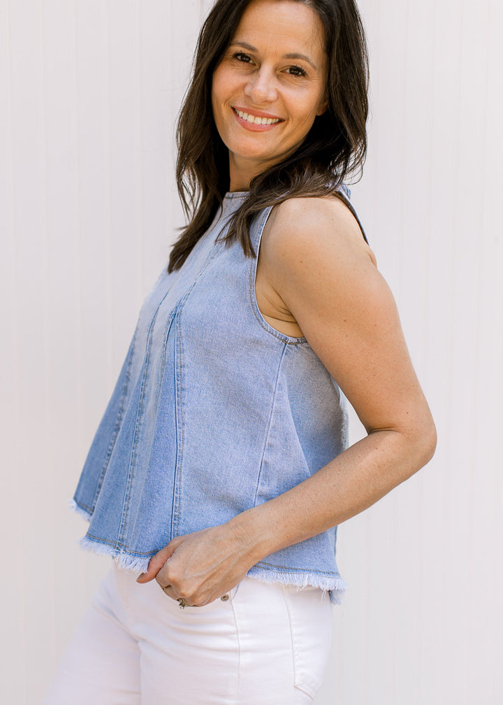 Model wearing a sleeveless lightwash denim top with a raw edge hem and a hidden back zipper. 