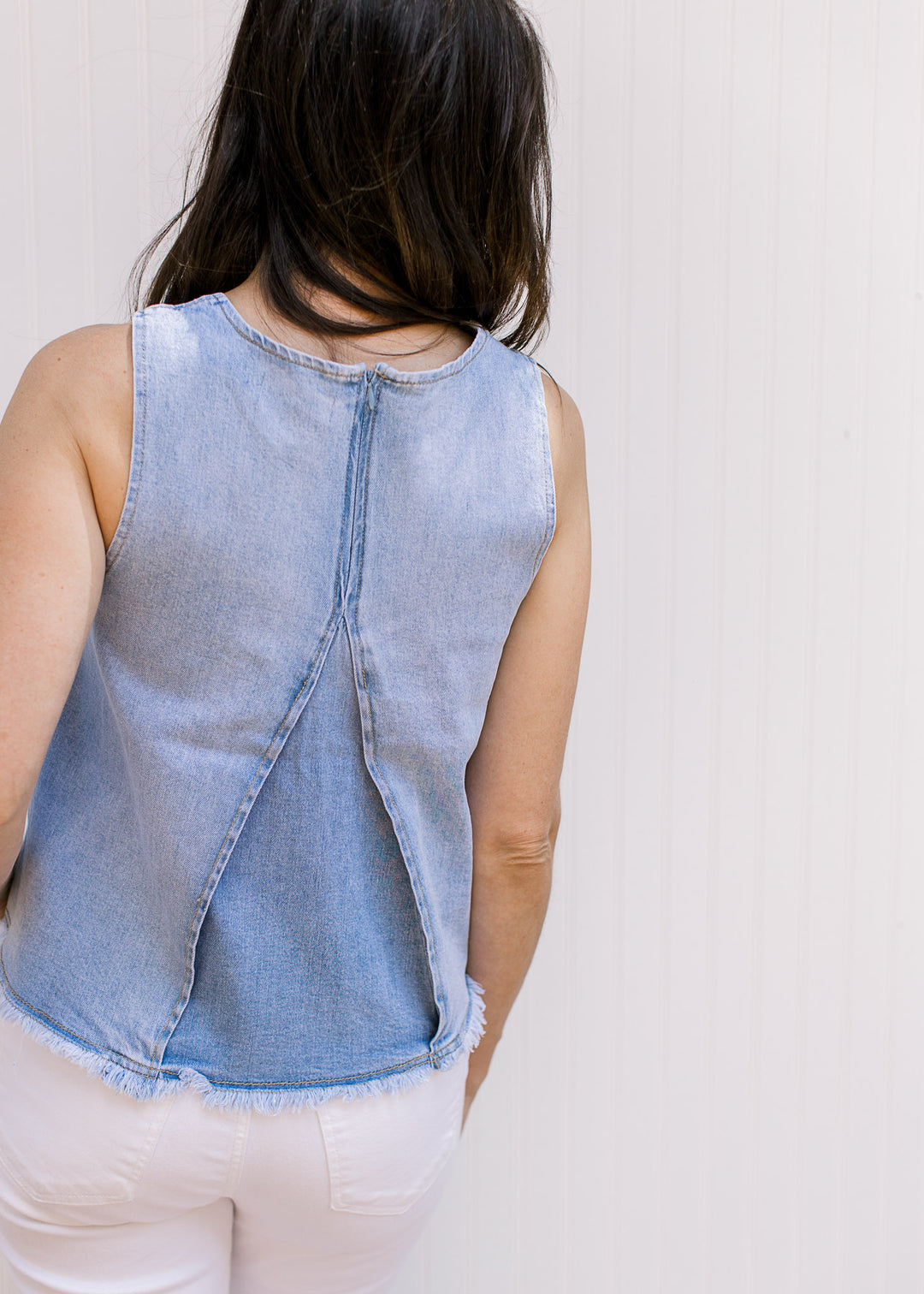 Back view of Model wearing a lightwash denim top with a raw edge hem and a hidden back zipper. 