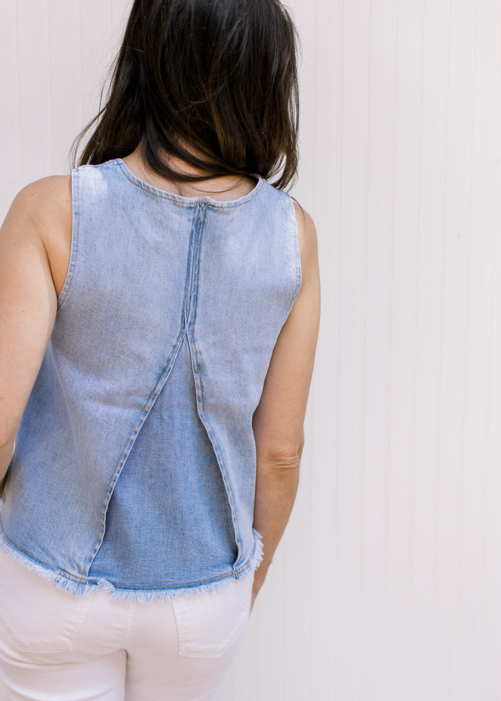 Back view of Model wearing a lightwash denim top with a raw edge hem and a hidden back zipper. 