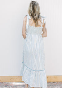 Back view of Model wearing a blue and cream striped maxi with blue piping and a smocked back. 