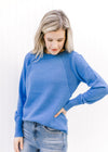 Model wearing a blue sweater with a ribbed detail at the shoulder, a crew neck and long sleeves. 