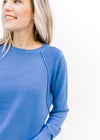 Close up of ribbed shoulder detail on a blue sweater with a crew neck and long sleeves. 