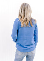 Back view of Model wearing a blue sweater with a ribbed detail at the shoulder and long sleeves. 