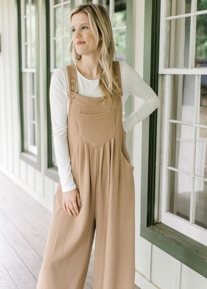 Model wearing a light brown jumpsuit with a ribbed material, adjustable straps and wide legs. 