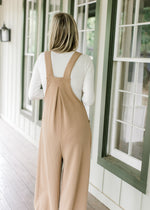 Back view of Model wearing a light brown jumpsuit with a ribbed material and wide legs. 