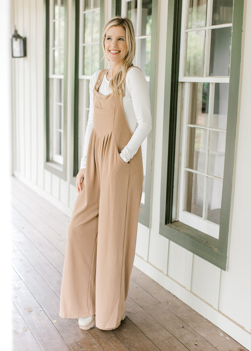 Model wearing a light brown jumpsuit with a ribbed material, pockets and wide legs. 