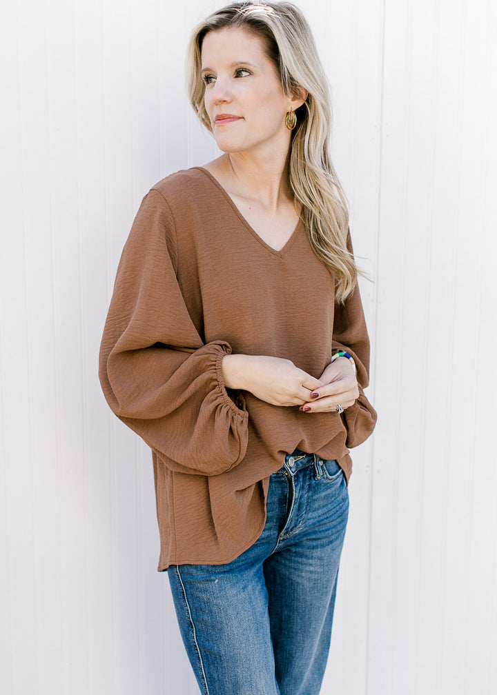 Model wearing a brown oversized v-neck top with 3/4 bubble sleeves and a polyester material. 