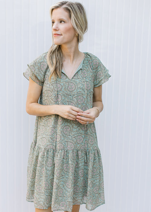 Model wearing a sage dress with paisley design, layered short sleeves and v-neck. 