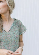 Come up of v-neck with a tie and layered short sleeves on a sage dress with paisley pattern.