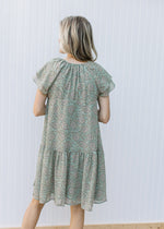 Back view of Model wearing a sage dress with paisley design, layered short sleeves and v-neck. 