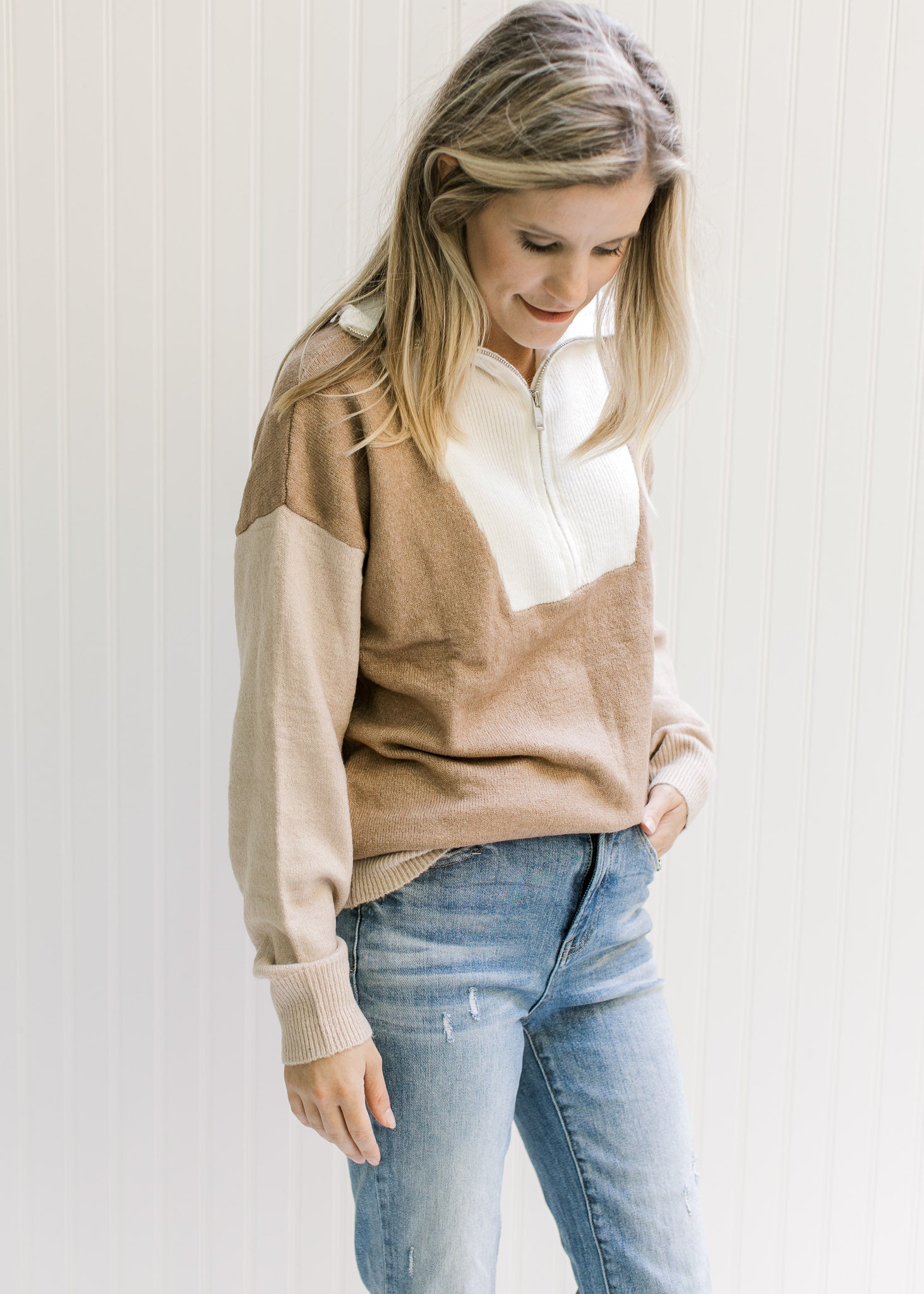Model wearing jeans with a cream, camel and taupe sweater with ribbed detail, turtleneck and zipper.
