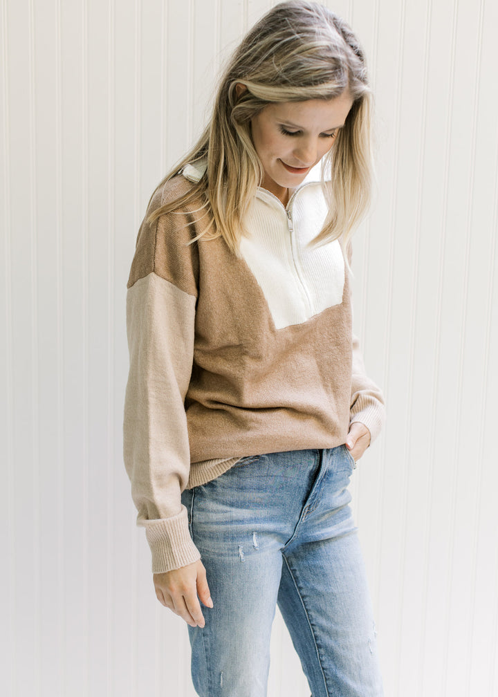 Model wearing jeans with a cream, camel and taupe sweater with ribbed detail, turtleneck and zipper.