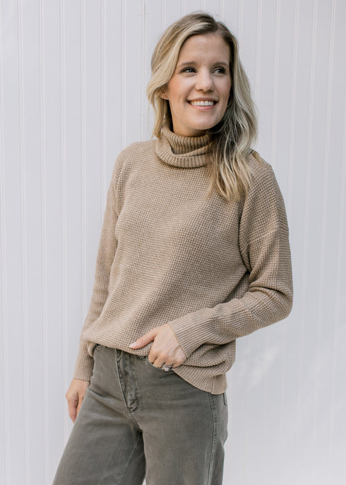 Model wearing a taupe sweater with a honeycomb pattern, loose turtle neck and long sleeves. 