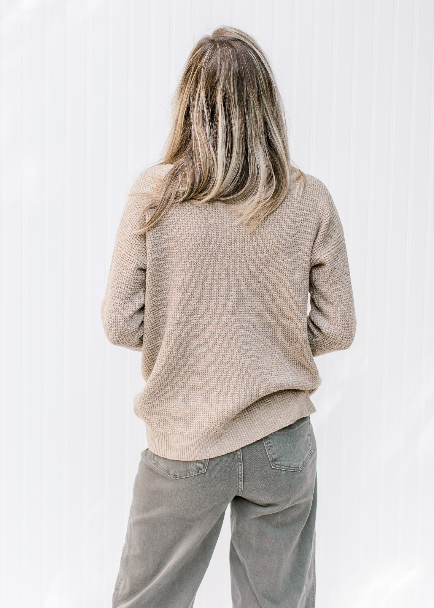 Back view of Model wearing a taupe sweater with a honeycomb pattern, turtle neck and long sleeves.