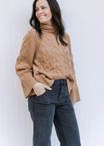 Model wearing jeans with a camel cable knit sweater with a turtle neck and long sleeves. 