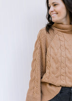 Model wearing a camel cable knit sweater with a turtle neck and long sleeves. 