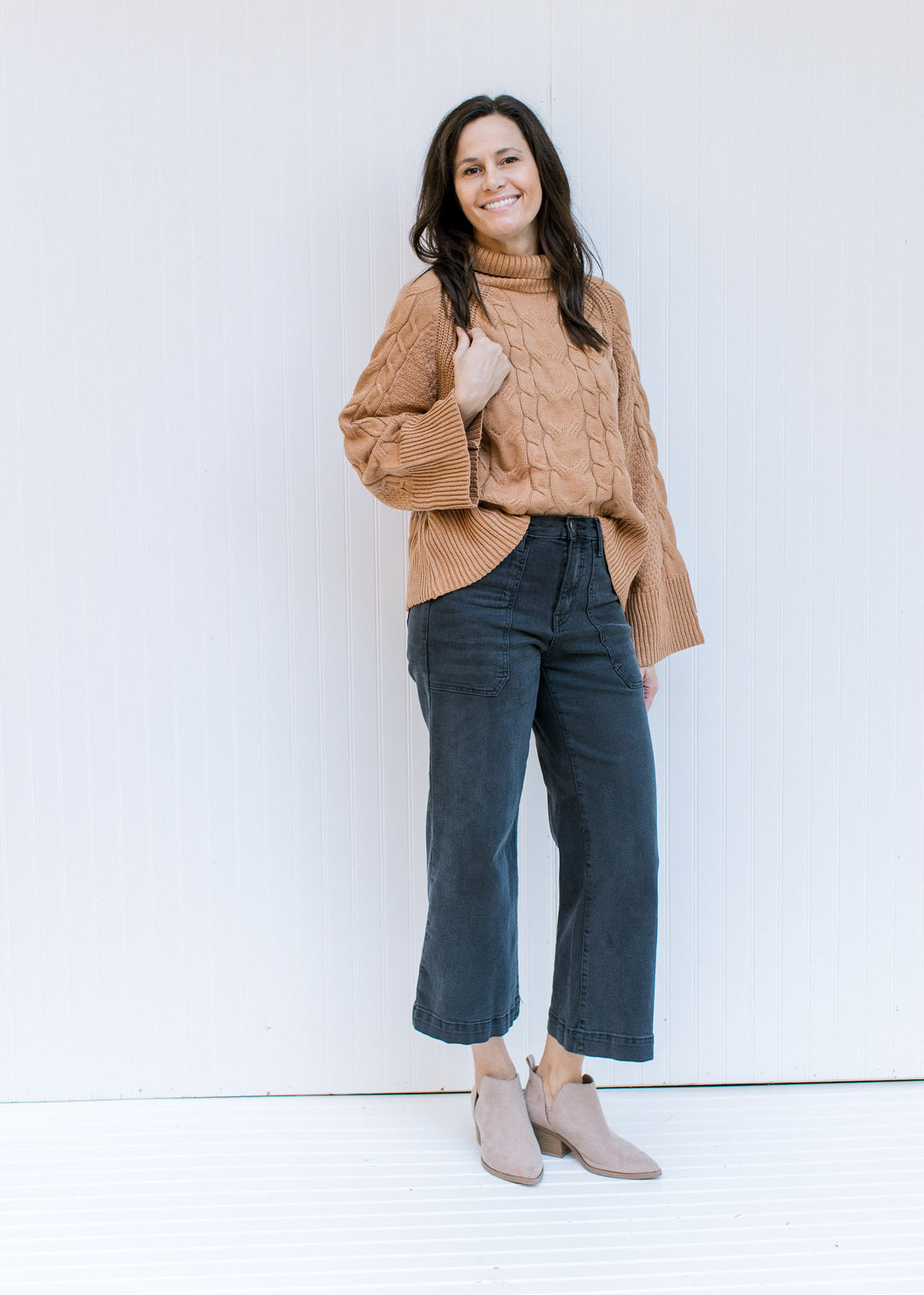 Model wearing jeans and booties with a camel cable knit sweater with a turtle neck and long sleeves.