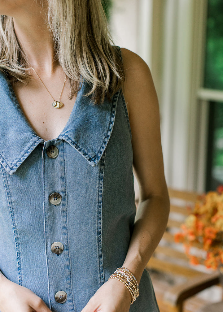 Close up of buttons and flap collar on a medium wash denim romper with a sleeveless design.