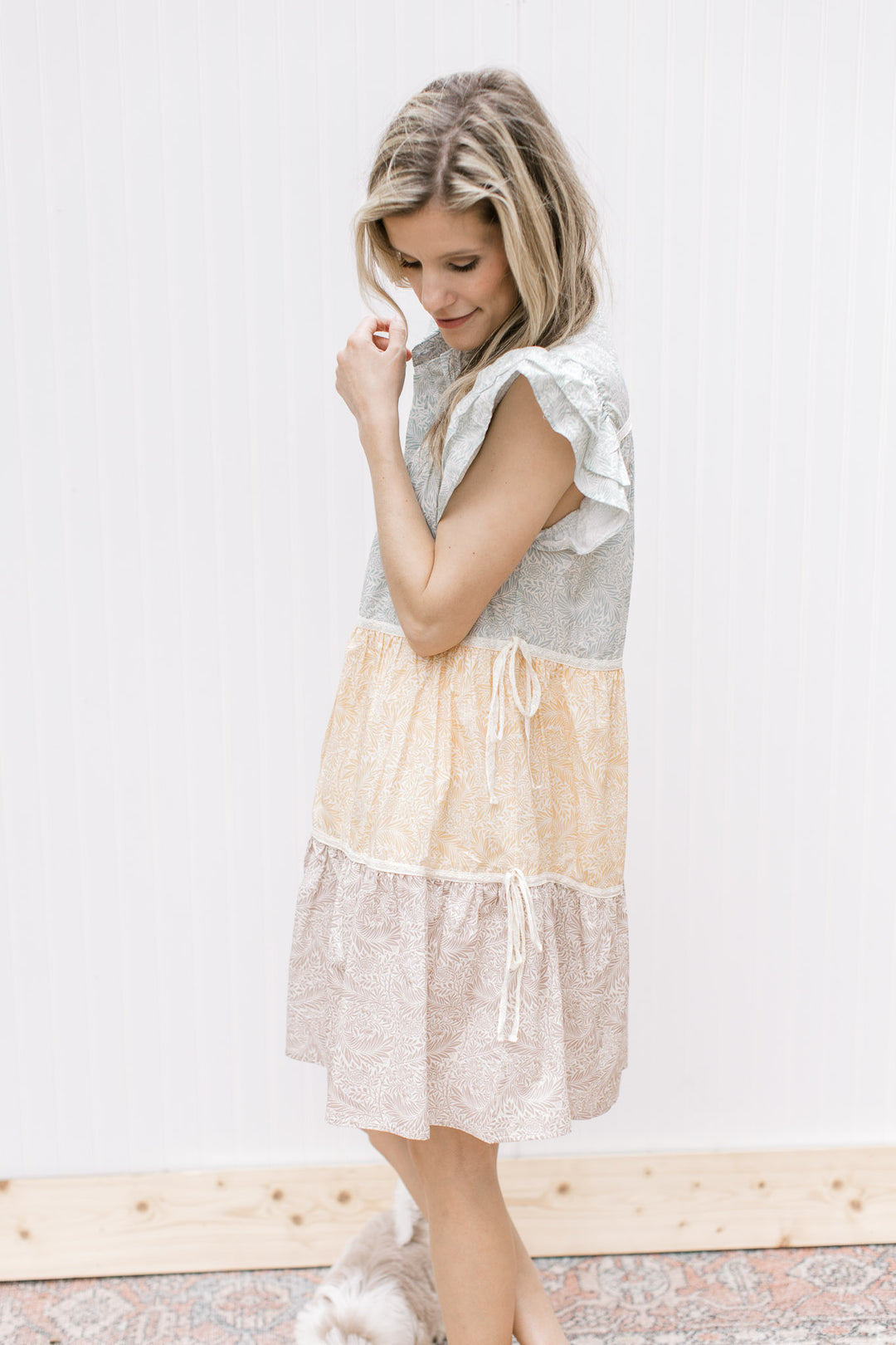 Side view of Model is wearing a sage, mustard and khaki floral dress with ruffle cap sleeves.