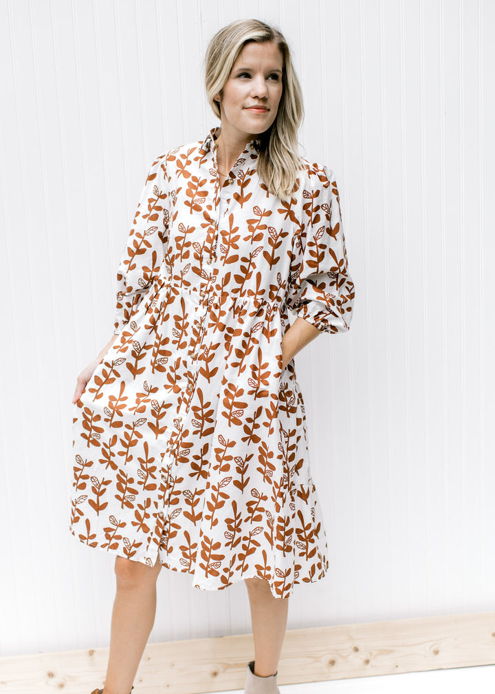 Model wearing a white midi dress with a brown leaf pattern, button front and bubble 3/4 sleeves. 