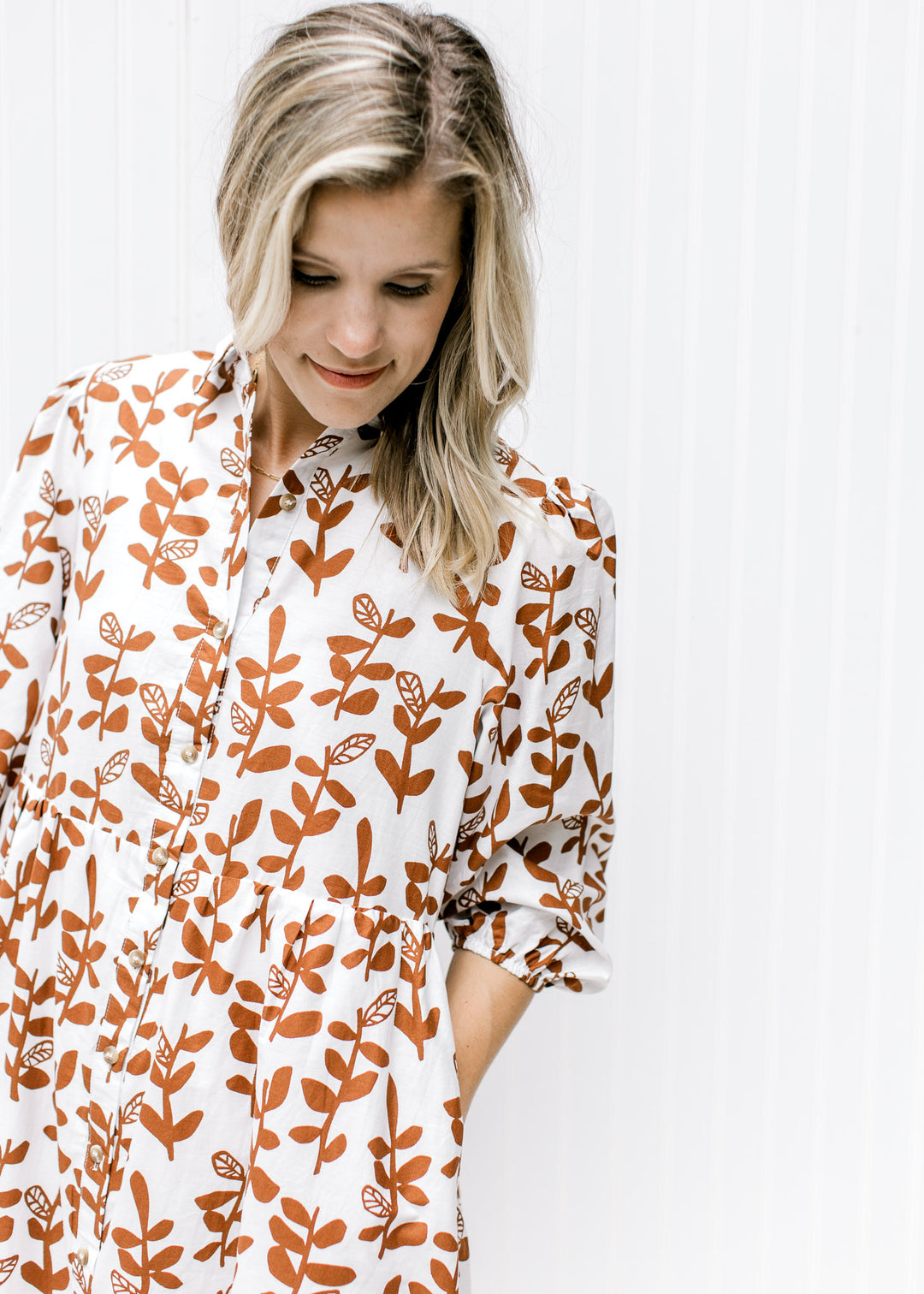 Close up of button closure and 3/4 bubble sleeves on a white dress with a brown leaf pattern. 