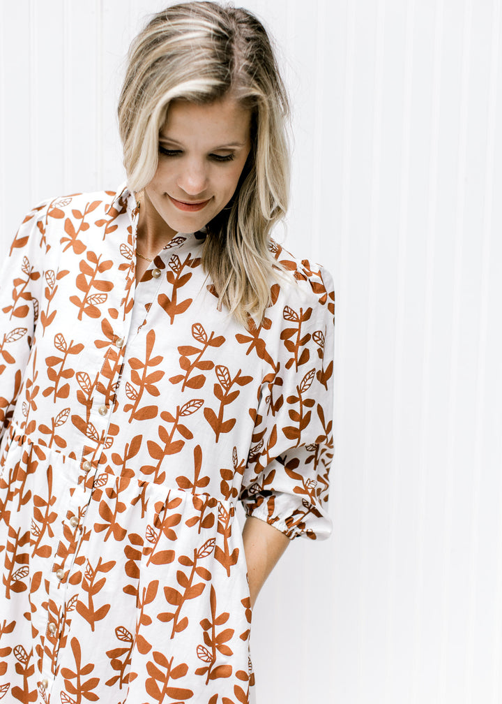 Close up of button closure and 3/4 bubble sleeves on a white dress with a brown leaf pattern. 