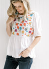 Model wearing an ivory babydoll top with embroidered floral pattern on bodice. 