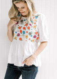 Model wearing an ivory babydoll top with embroidered floral pattern on bodice. 