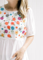 Close up view of embroidered floral pattern on a ivory babydoll top with bubble short sleeves. 