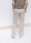 Back view of Model wearing tan wide leg pants with pockets, rayon material and a tie at the waist. 