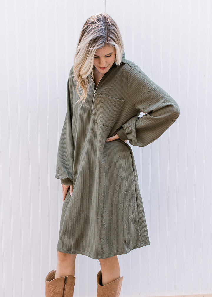 Model wearing an olive ribbed midi with a quarter zip neck, long sleeves and a patch pocket. 