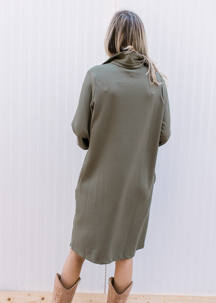Back view of Model wearing an olive ribbed midi with a collar, long sleeves and a patch pocket. 
