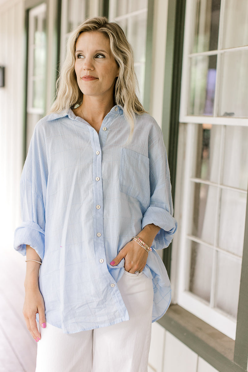 Model wearing white pants with a light blue button down top with a patch pockets and long sleeves. 