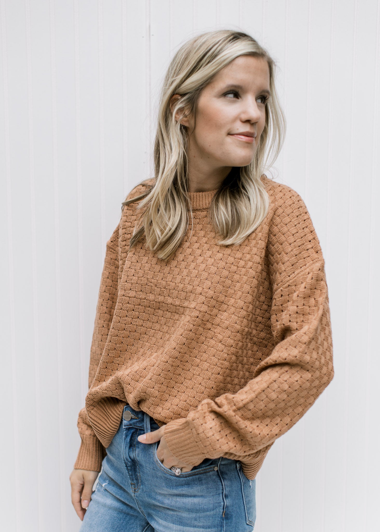 Model wearing a copper colored sweater with a basket weave stitch, long sleeves and acrylic material