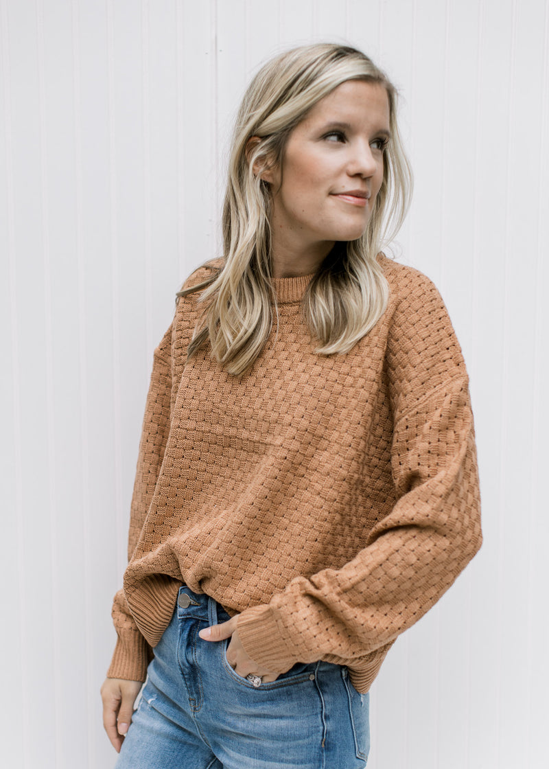 Model wearing a copper colored sweater with a basket weave stitch, long sleeves and acrylic material