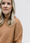 Close up of basket weave stitch on a copper colored sweater with long sleeves and acrylic material. 