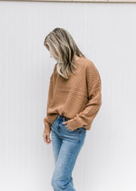 Model wearing jeans and a copper colored sweater with a basket weave stitch and long sleeves. 