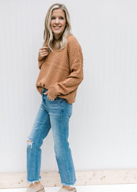 Model wearing jeans, mules and a copper colored sweater with a basket weave stitch and long sleeves.