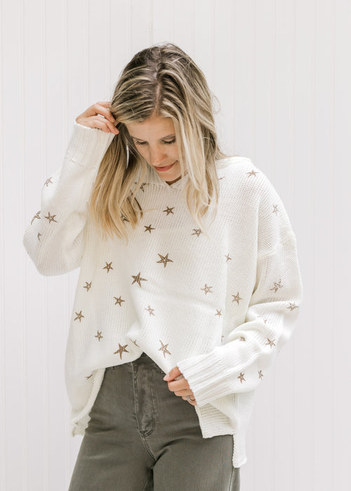 Model wearing a cream v-neck sweater with copper colored stars and long sleeves.