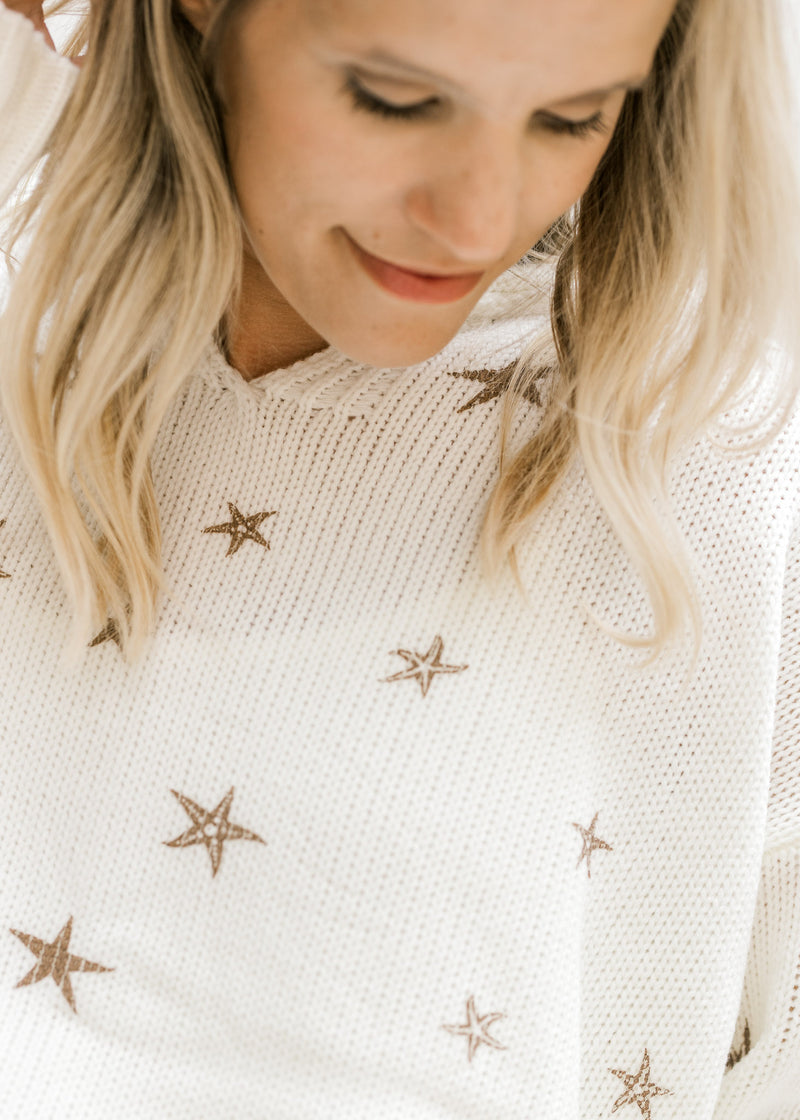Close up view of copper colored stars and v-neck on a acrylic cream sweater. 