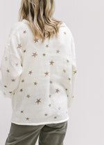 Back view of Model wearing a cream v-neck sweater with copper colored stars and long sleeves.