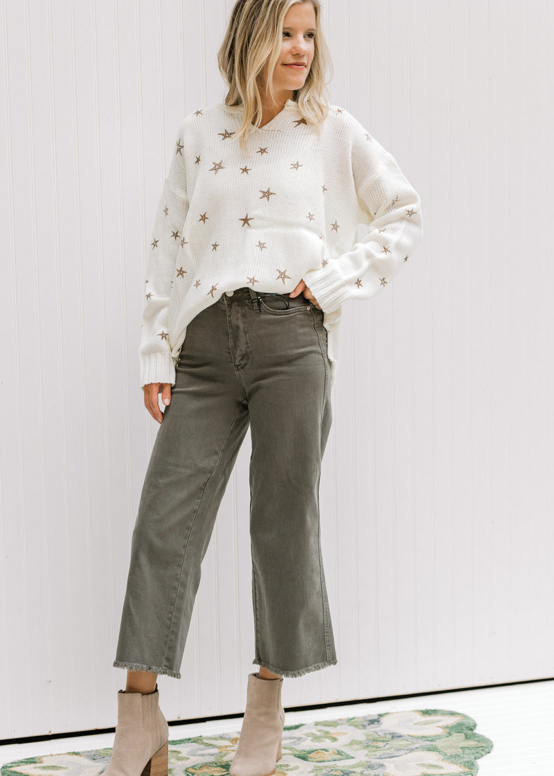 Model wearing gray jeans with a cream v-neck sweater with copper colored stars and long sleeves.
