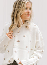 Model wearing a cream sweater with a copper stars pattern and long sleeves, tucked into gray jeans.