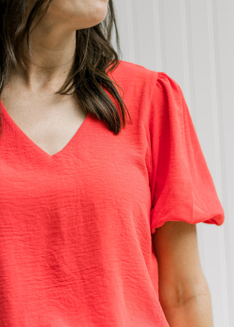 Close up view of v-neck and bubble short sleeves with a pleated shoulder on a coral top. 