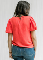 Back view of Model wearing a coral top with bubble short sleeves, pleated shoulder and v-neck. 