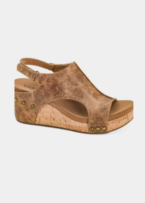 Side view of a cognac wedge with 3” heel to 1” platform, a slip-on design and adjustable strap. 