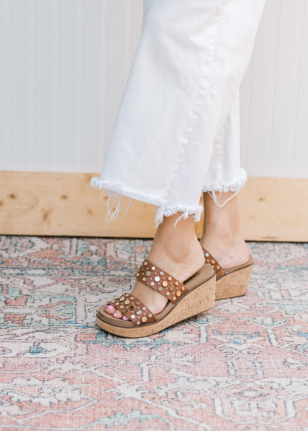 Side view of model in a brown double strap wedge with metal embellishments and slip-on design. 