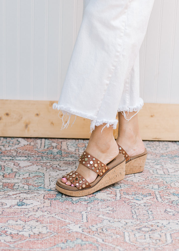 Side view of model in a brown double strap wedge with metal embellishments and slip-on design. 