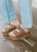 Model wearing dark brown chunky stacked sandal with studded sides, and gold buckle.